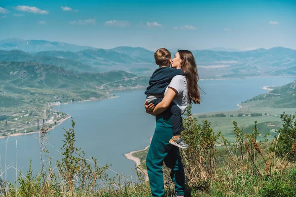 Mor med son på händerna står mot blått hav och berg bakgrund — Stockfoto