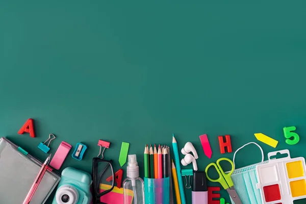 Office stationery with medical mask and headphones on green background.