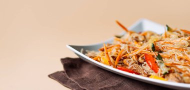 Kare tabakta spagetti ve arka planda et salatası.