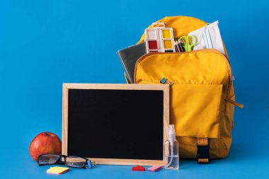 Mavi arkaplanda sarı sırt çantası ve tebeşir tahtası.