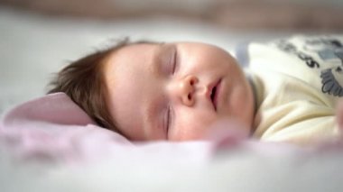 Bebek yatakta uyuyor. Ağzını emme refleksiyle oynatıyor.