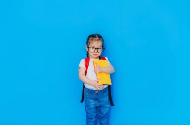 Okul konseptine geri dönelim. Kırmızı sırt çantalı ve mavi arka planda sarı klasörlü kız..