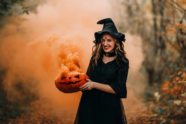 Cadı gibi giyinmiş gülümseyen kız elinde buharlı balkabağı tutuyor. — Stok fotoğraf