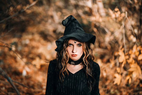 Portrait of girl in witch costume in front of the forest.