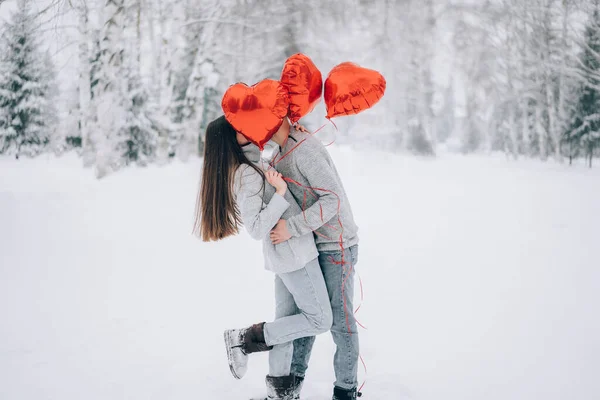 若い夫婦は雪の公園でキスをし ハート型の風船の後ろに隠れて — ストック写真