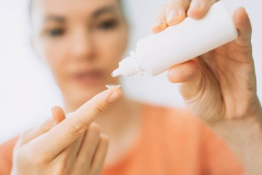 Genç kız parmağında görme için lens tutuyor ve içine göz damlaları damlatıyor..