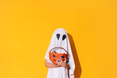 Hayalet kostümlü çocuk elinde şekerli balkabağı sepeti tutuyor..