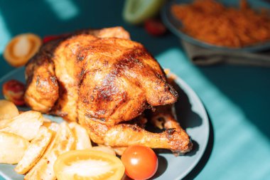 Mavi tabakta taze ızgara tavuk ve mavi arka planda patates ve domates.