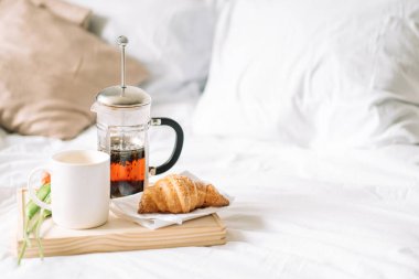 Ay çöreği ve çay beyaz yatakta hasır tepside çiçeklerle.