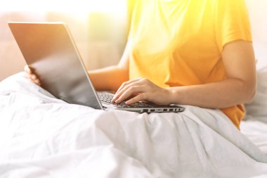 Yatakta oturan ve dizüstü bilgisayarda çalışan kız..