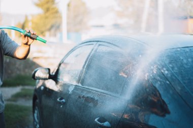 Elinde hortum olan adam arabanın üzerine su döker.