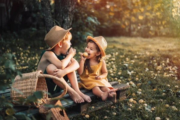 Дети в комбинезонах и соломенных шляпах едят грушу — стоковое фото