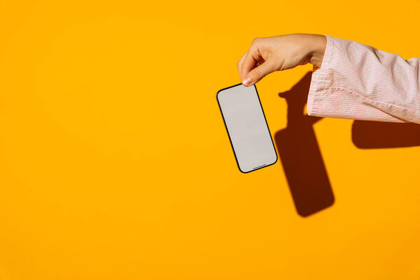 Рука держит современный смартфон с чистым экраном на ярком желтом фоне. Высокое качество фото