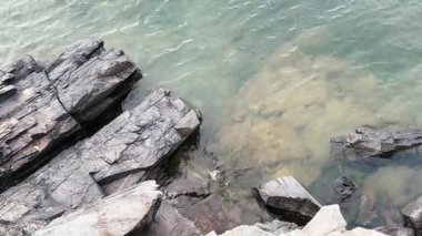 Karanlık kıyı kayaları ve küçük dalgalarla çevrili berrak su. Yüksek kalite 4k görüntü