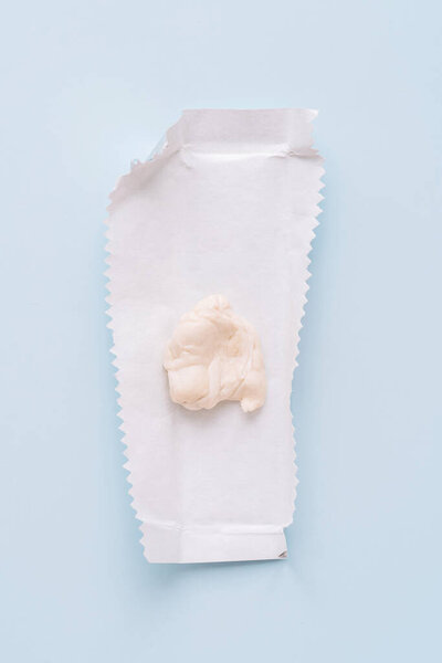 Chewed chewing gum on opened wrapper on blue background, minimal flat lay. High quality photo