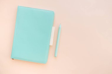 Turkuaz defter, pastel arka plan, planlama ve günlük konsepti üzerine kalem ve yapışkan bir notla açıyla yerleştirilmiş, kopyalama alanı.