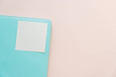 Bir turkuaz defter köşesine yakın plan, pastel arka planda boş yapışkan bir not, büyük kopya alanı olan en küçük kırtasiye konsepti.