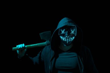 Man armed with an axe and wearing a scary lighting neon glow mask and a hoodie on black background. clipart