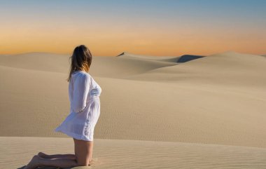 Beyaz elbiseli güzel bir kadın ve çölde siyah kum tepeciği..