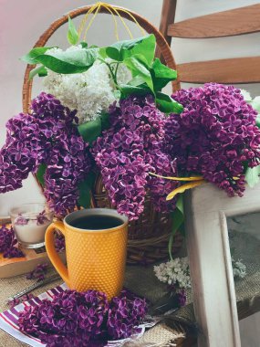 Sepette leylakla dolu bir hayat, sarı bir bardak, pencerenin kenarında bir kitap ve mum.