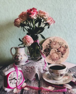 Bir buket pembe gül. Bir fincan kahve. Saat. Vintage. Yeşil bir duvarın arkası..