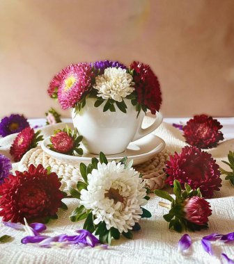 Sonbahar çiçekleri. Asterlar. Beyaz, pembe, kırmızı, mor renkler. Masada bir fincan ile durgun bir hayat.