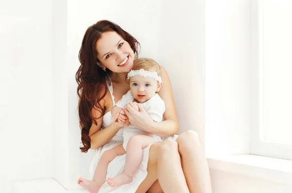 Gelukkig lachend moeder met baby thuis in witte kamer in de buurt van venster — Stockfoto