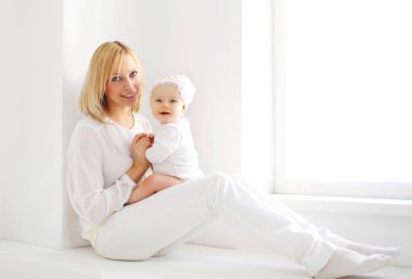 Anne ve bebek evde pencere yakınındaki beyaz odada gülümseyen mutlu