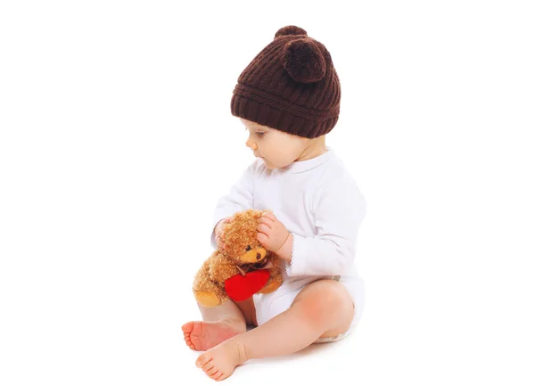 Baby in knitted brown hat with teddy bear toy sitting on white b — Stock Photo, Image