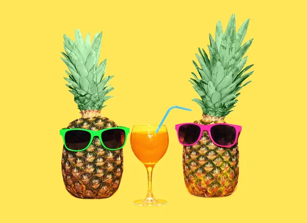 Due ananas con occhiali da sole e succo di frutta di vetro su ba gialla — Foto Stock