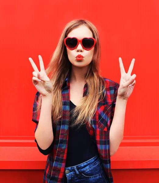 Mujer bonita en gafas de sol rojas soplando labios beso sobre colorido b — Foto de Stock