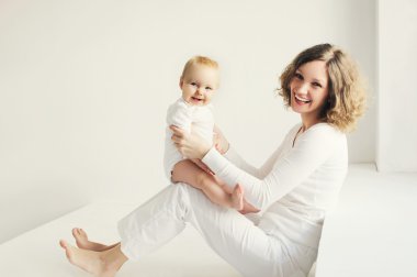 Mutlu gülümseyen anne beyaz odada bebekle oynuyor.