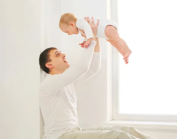 Pai feliz brincando com o bebê em casa na sala branca perto da janela — Fotografia de Stock