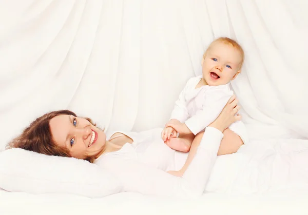 Gelukkig lachend moeder spelen met baby liggend op bed thuis — Stockfoto