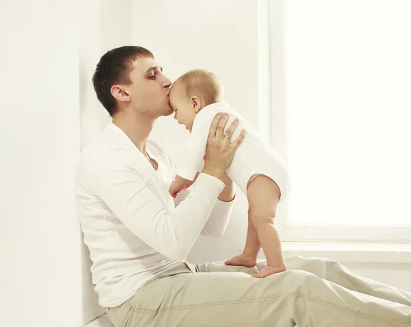 Glücklicher junger Vater küsst Baby zu Hause in weißem Zimmer in der Nähe von windo — Stockfoto