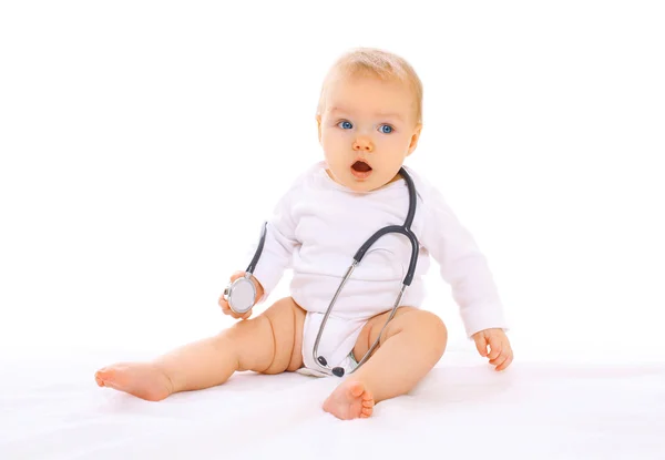 Baby playing with stethoscope sitting on white background Stock Picture