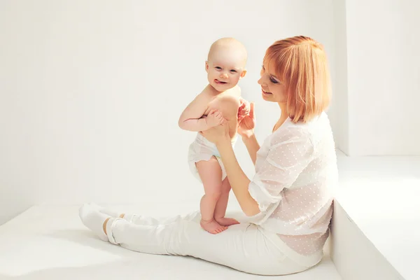 Feliz sonriente madre jugando con bebé casa en blanco habitación cerca w —  Fotos de Stock
