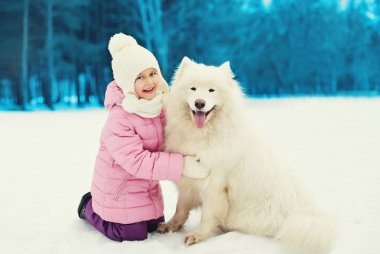 Beyaz Samoyed köpek ile kablosuz karda oynarken mutlu gülümseyen çocuk