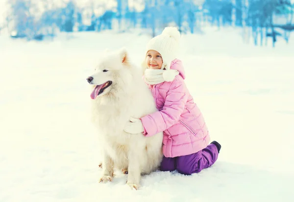 Lyckligt barn med vita samojed hund spelar på snö i vinterdag — Stockfoto