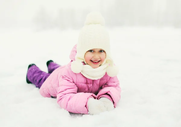 Gelukkig lachend klein meisje kind liggend op sneeuw in de winterdag — Stockfoto