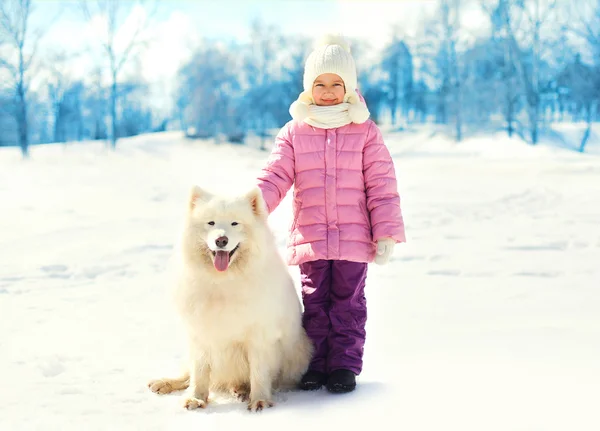 Litet barn med vita samojed hund på snö i vinter park — Stockfoto