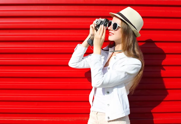 Mujer bonita con cámara retro disparando sobre fondo rojo — Foto de Stock