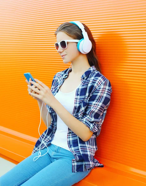 Donna in cuffia ascolta la musica utilizzando smartphone su colore — Foto Stock