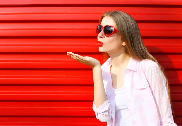 Femme en lunettes de soleil rouges envoie un baiser d'air sur backgrou coloré — Photo