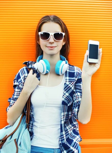 Женщина показывает экран смартфона в наушниках и солнцезащитных очках — стоковое фото