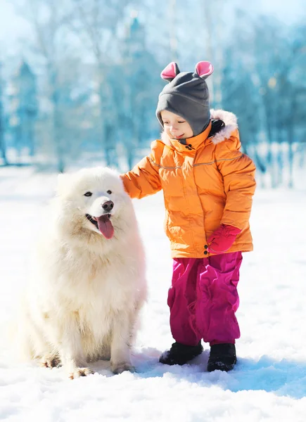 Glimlachend kind met witte Samojeed hond op sneeuw in de winter park — Stockfoto