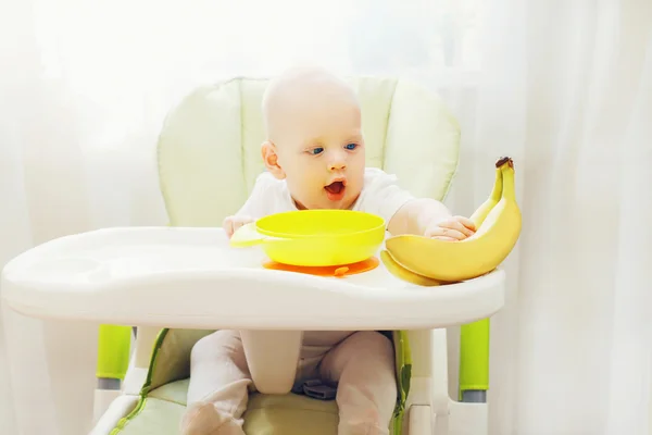 Baby sitting at the table home and takes fruits bananas