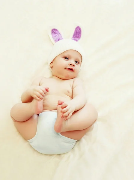 Bebê bonito em chapéu de malha com orelhas de coelho deitado na cama em casa — Fotografia de Stock