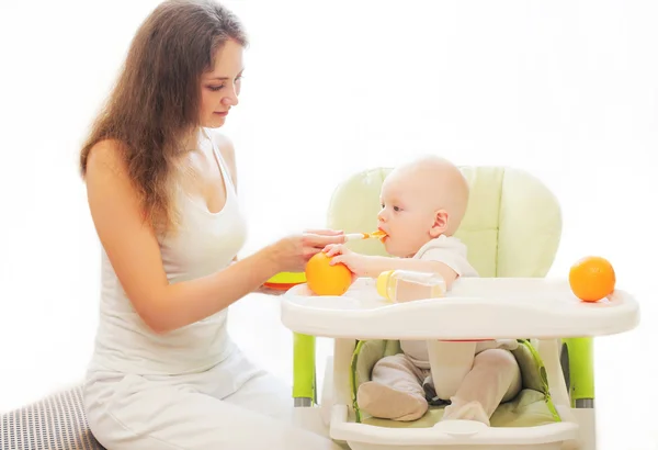 Matka krmí malé baby lžíce na stole doma — Stock fotografie