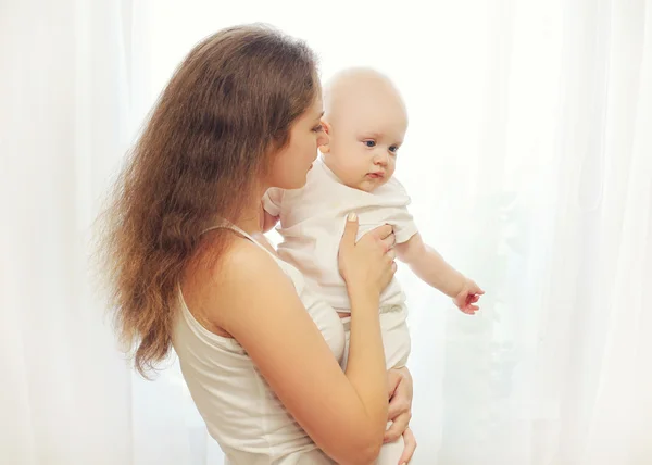 Retrato mãe abraçando seu bebê sobre branco janela — Fotografia de Stock